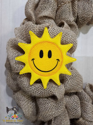 A felt sun design with a smiling face and sun rays, intended for use as a wreath decoration.