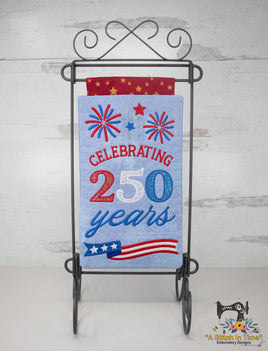 Decorative banner with 'Celebrating 250 years' text and American flag design on a stand against a light wooden background.