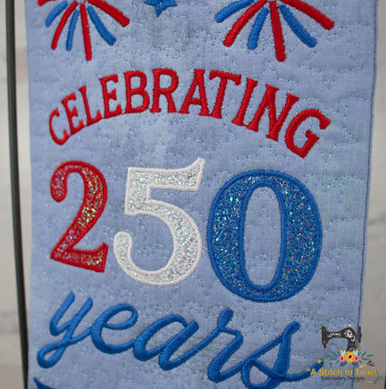 Embroidered fabric with 'Celebrating 250 years' text on a blue background with red and blue elements.
