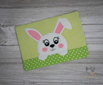 A green fabric mug rug with a white bunny applique and pink polka dots on a white background.