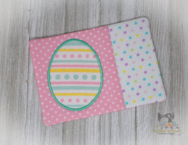 A digital image of an embroidery design file for an egg-shaped mug rug with a polka-dot and striped pattern on a white background, and a sample physical mug rug with the same design on a wooden surface.
